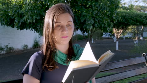 young caucasian student woman slowly turns page of book outdoors