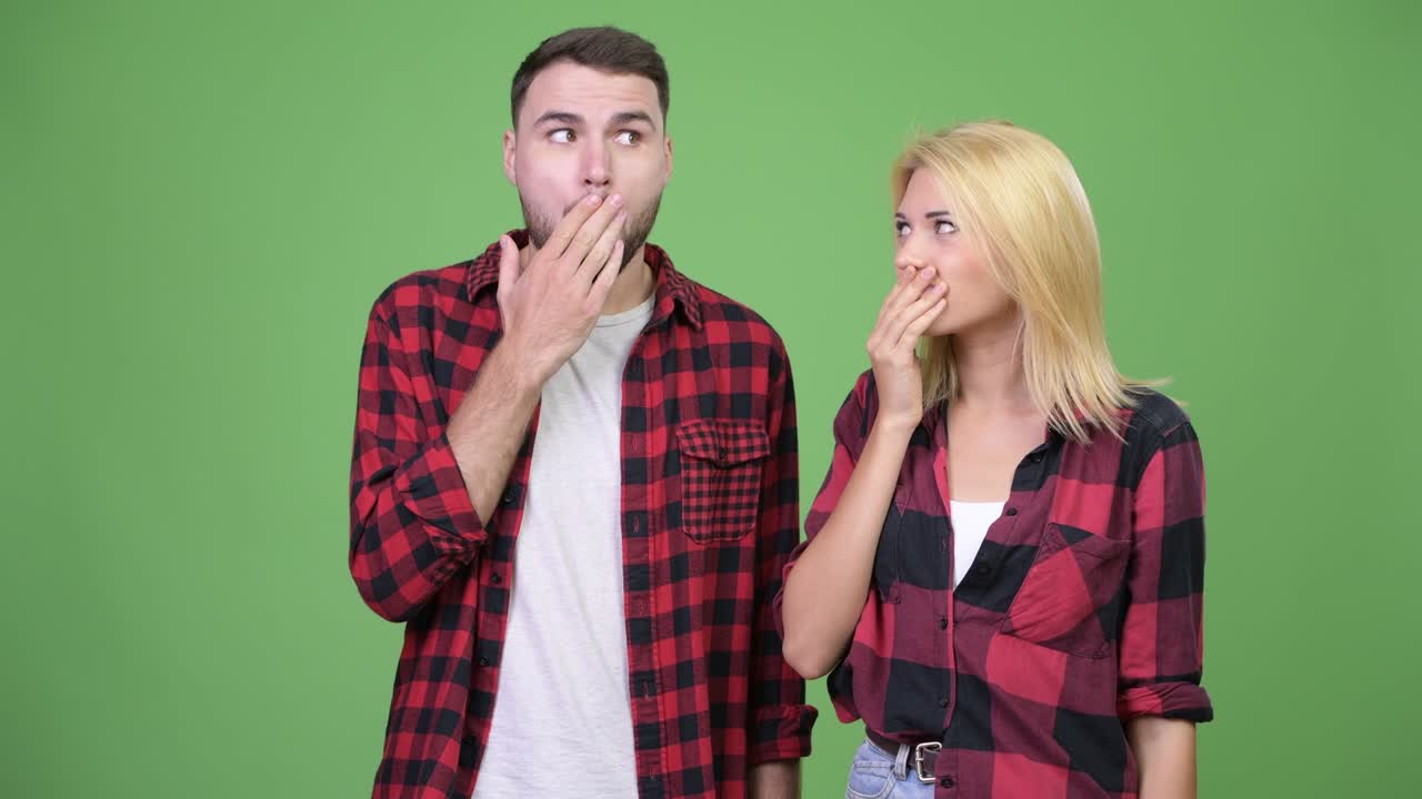 Young couple covering mouth together while looking guilty