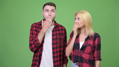 young couple covering mouth together while looking guilty