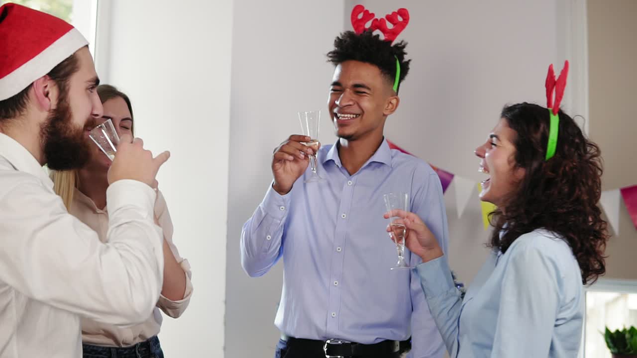 multi ethnic group of young office workers clicking glasses with sparkling wine wearing christmas hats and celebrating Christmas