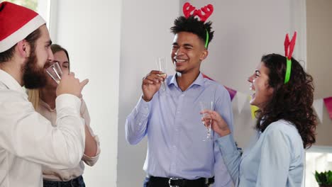 multi ethnic group of young office workers clicking glasses with sparkling wine wearing christmas hats and celebrating christmas