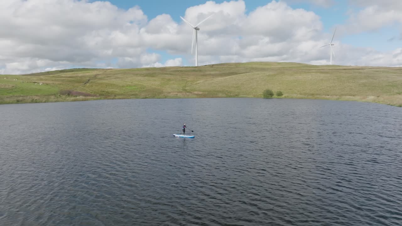 primer plano circular de un individuo en un sup con molinos de viento girando en el fondo