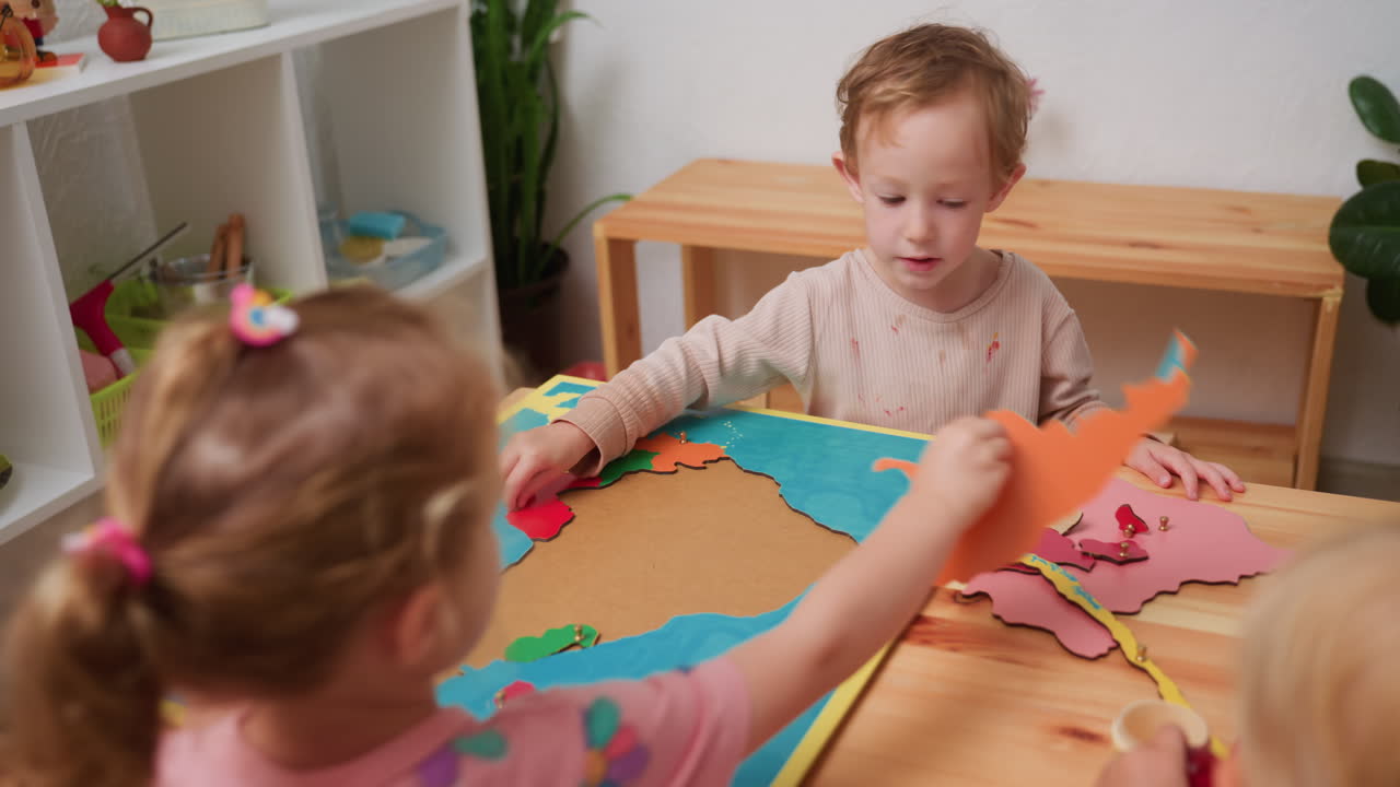 Niños en edad preescolar mueven piezas de puzles de continentes del tablero del mapa a un lado, practicando geografía y habilidades motoras finas en un aula Montessori luminosa, mesas de madera, estanterías, plantas, aprendizaje colaborativo