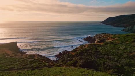 evening surf washing hills with low greenery. calm water rolling sunny cliffs