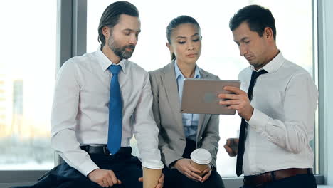 Dos-Hombres-De-Negocios-Y-Una-Mujer-De-Negocios-Con-Trajes-De-Oficina-Y-Hablando-En-Una-Videollamada-Usando-Una-Tableta