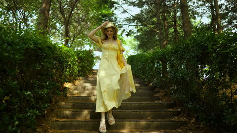 beautiful ukrainian woman in long yellow dress and summer hat walking down the stairs in the park