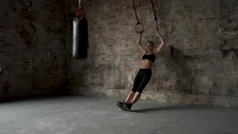 mujer joven en forma haciendo estiramientos en anillos de gimnasia. joven atleta musculosa haciendo ejercicios con anillos en el gimnasio. mujer joven en condiciones haciendo pull-ups en anilos de gimnasia