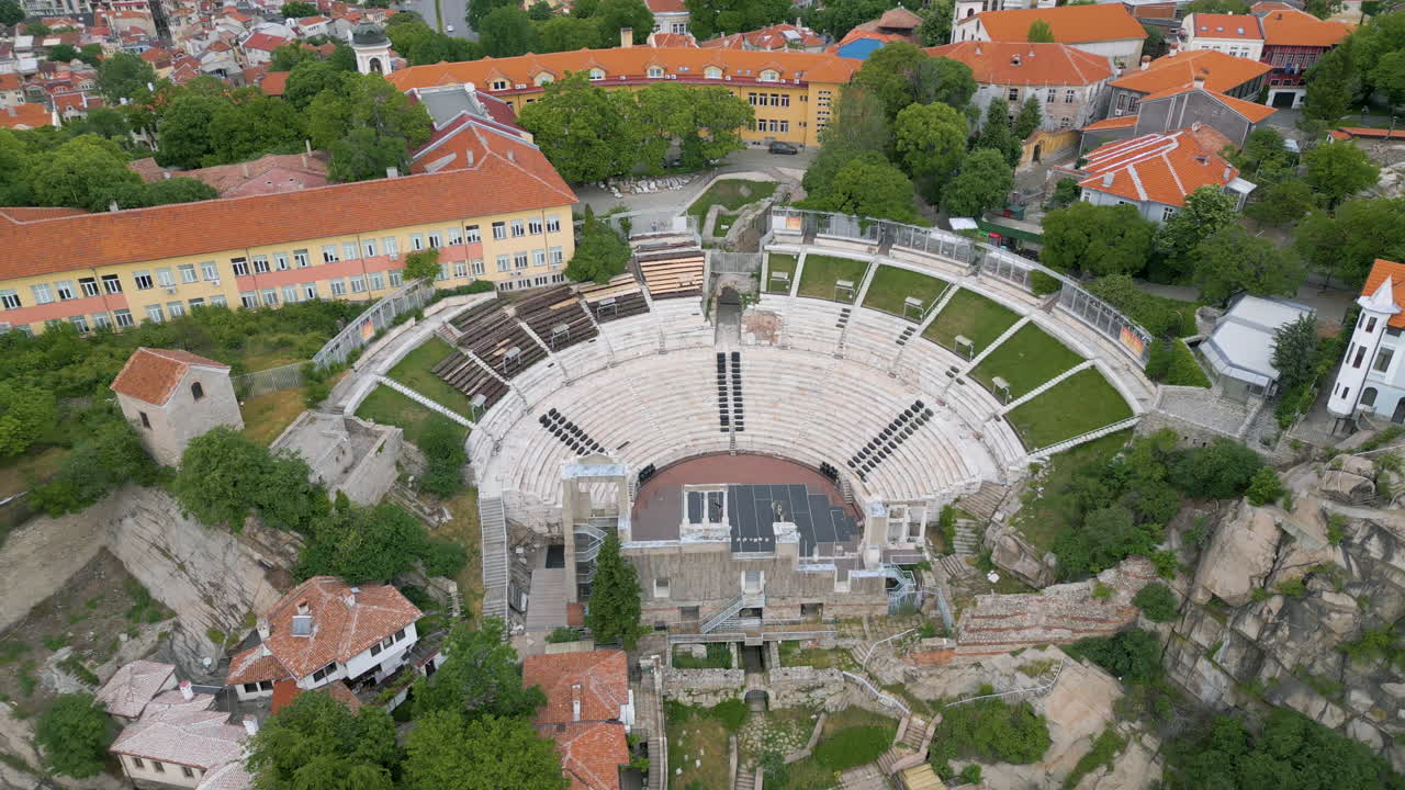 A top-down drone shot of the Ancient Roman Theater in Plovdiv, Bulgaria, showing the full semicircular structure on an early spring morning