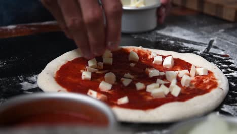 chef poniendo queso mozzarella en pizza de masa fermentada casera con salsa