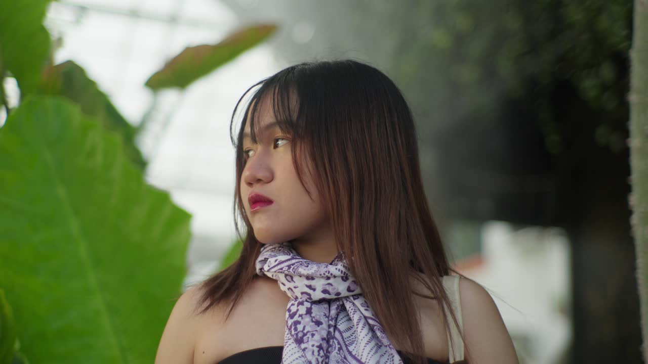 Young woman in a tropical garden looks thoughtfully to the side in soft lighting
