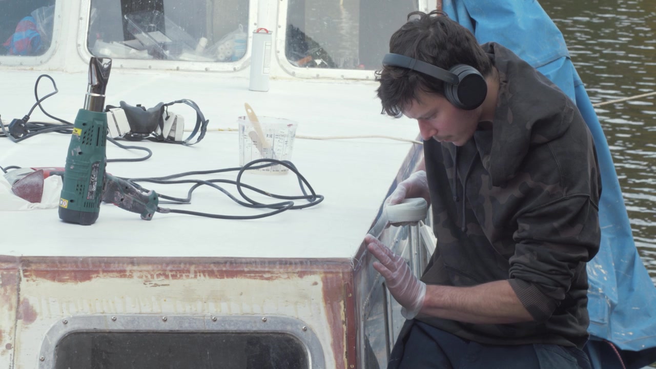 Man applying fiberglass (fibreglass) strip to boat cabin edge