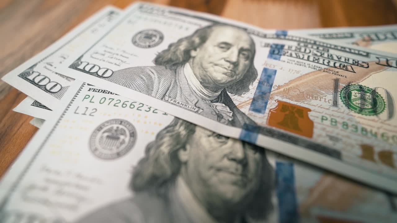 Notas de cem dólares caindo umas sobre as outras em câmera lenta, close-up.