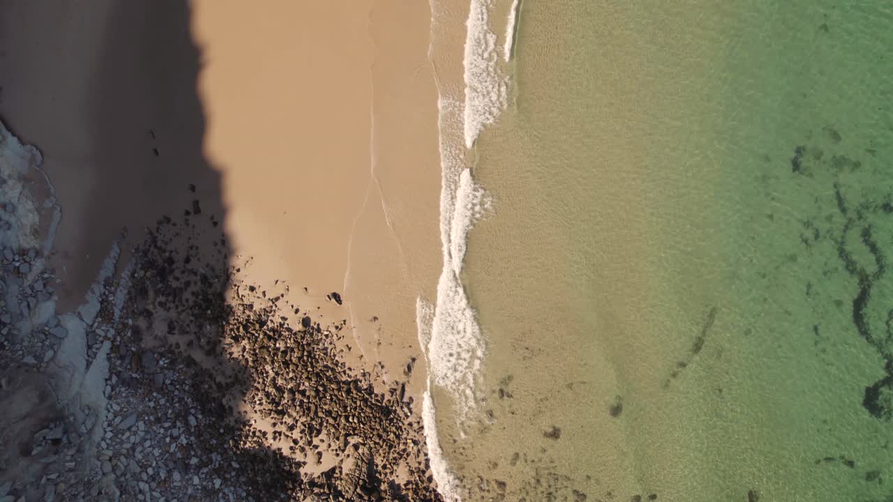 Vista aerea dall'alto, onde che si infrangono su una spiaggia di sabbia a Burgau, Algarve