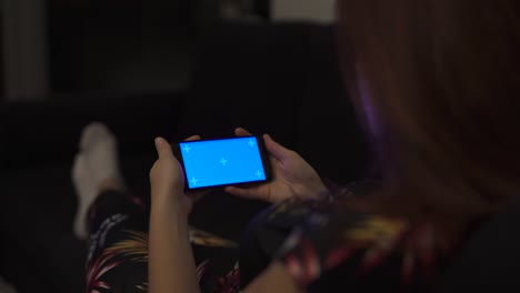chica atractiva viendo vídeo de pantalla simulada azul en el sofá en casa en modo paisaje horizontal, viendo películas, marcadores de seguimiento. viendo contenido, videos, blogs. 4k uhd.