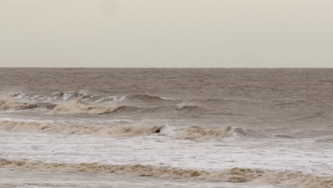 cold-bleak-looking-winter-waves-breaking-on-to-Ingoldm-musicells,-Skegness-sandy-beach