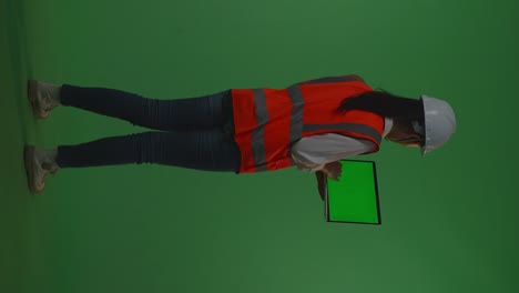 back view of full body asian female engineer with safety helmet working on a green screen laptop while standing in the green screen background studio, during sunset or sunrise time