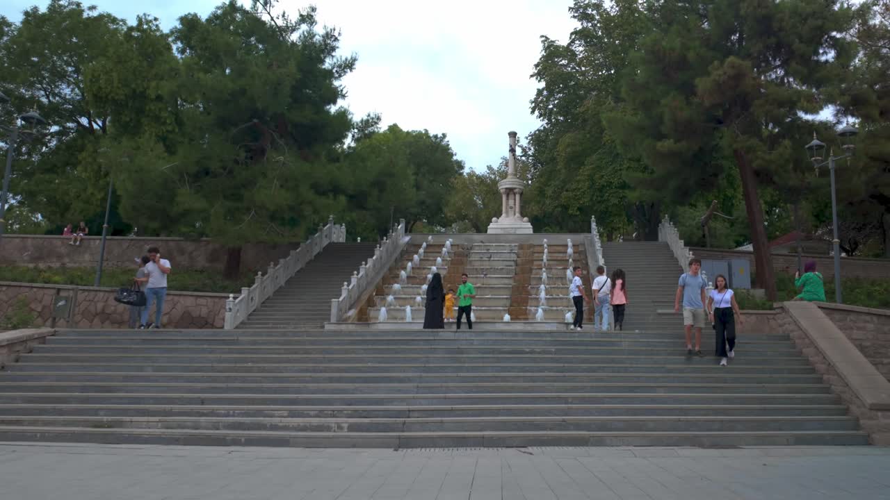 People Walking Up and Down Stone Steps with Fountains and Monument in a Park