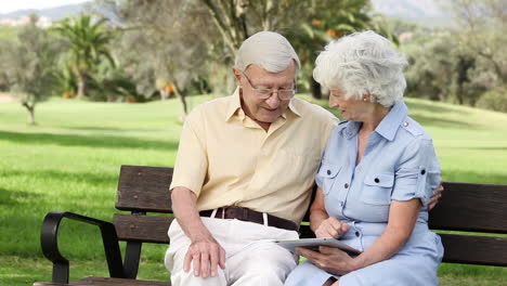 una pareja de ancianos usando una tableta en un banco