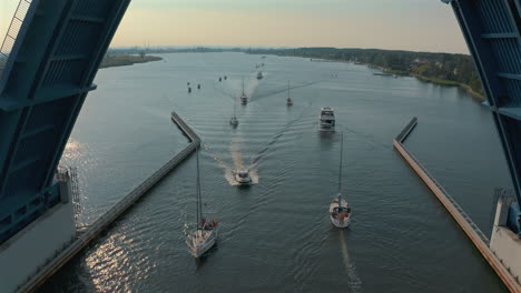 drone flying through opening bridge in sobieszewo, gdańsk with passing boats at the sunset