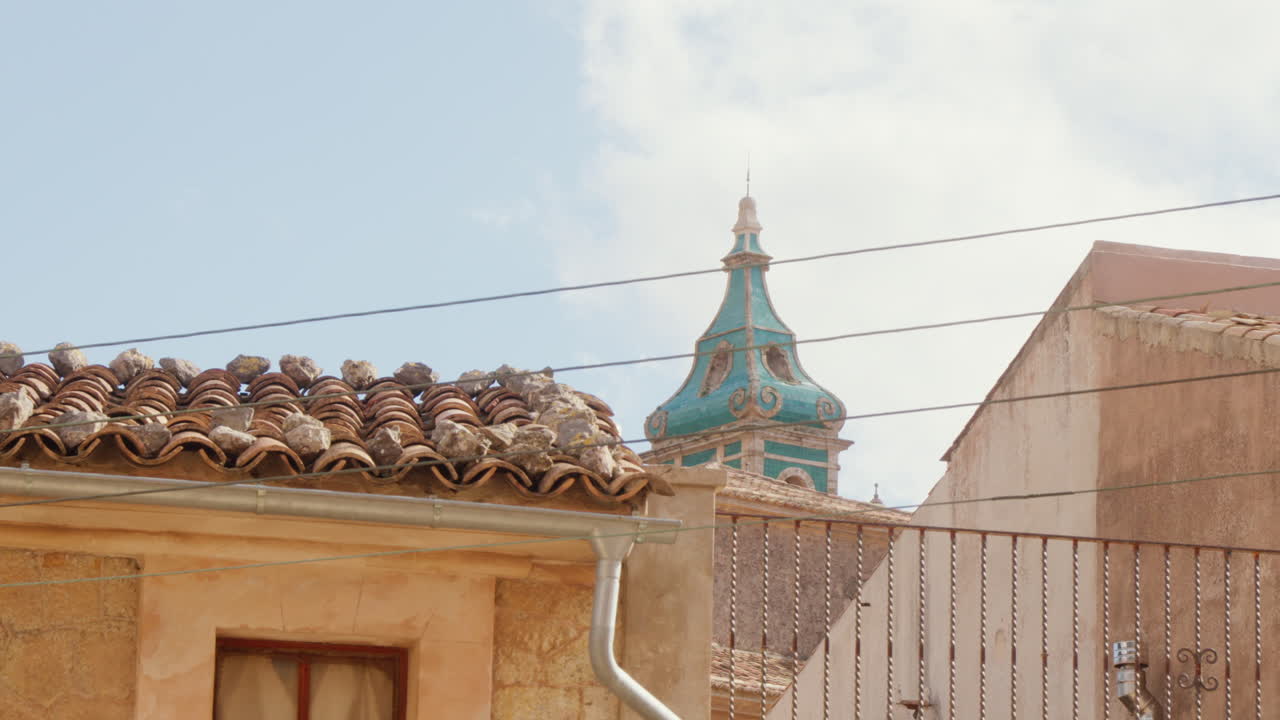 The steeple of a church stands tall against a clear blue sky in Valldemossa, Mallorca, Spain