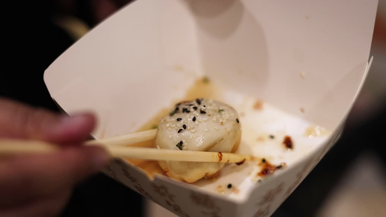 Mano che tiene le bacchette con un singolo raviolo ripieno di brodo in un contenitore di carta