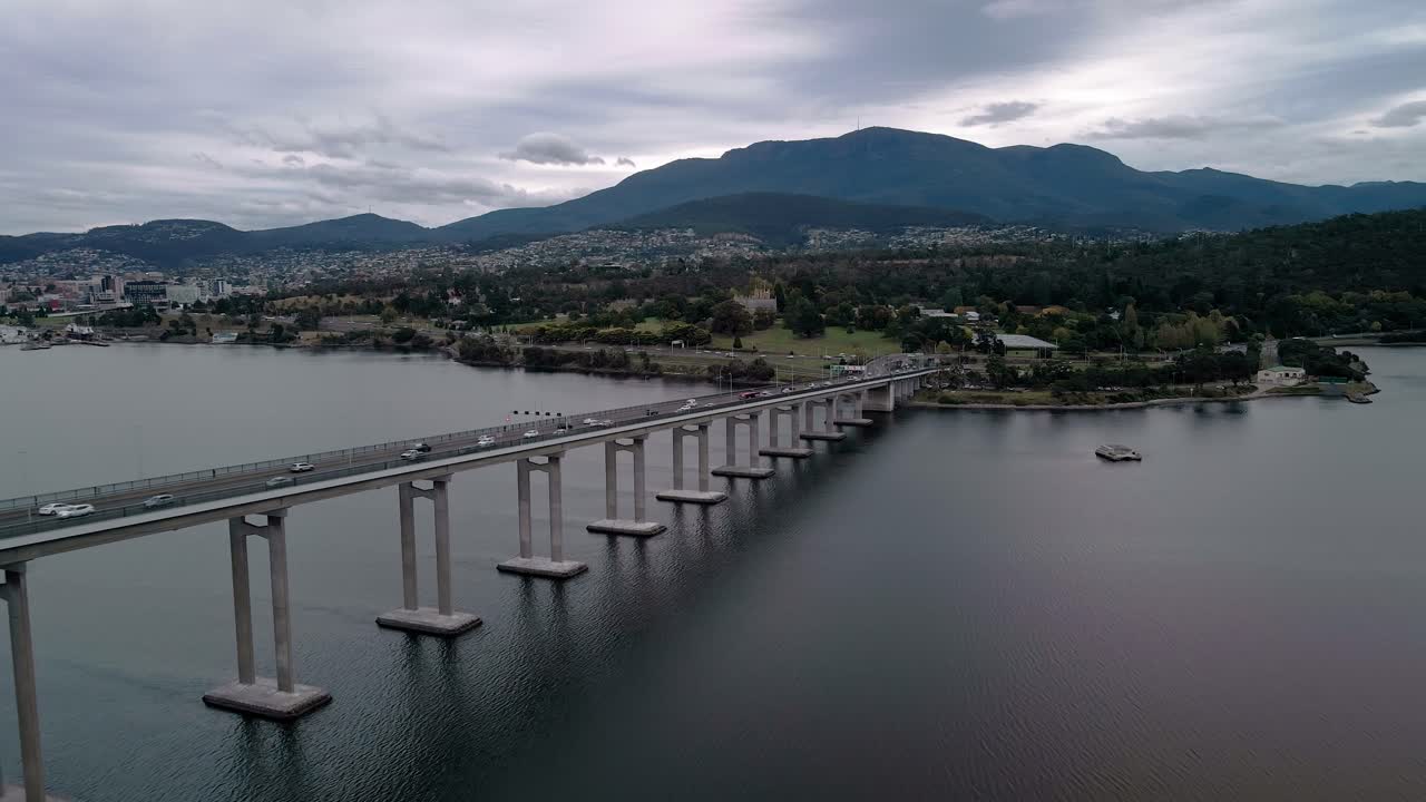 vista de perfil de un puente con paisaje urbano y montañas en el fondo en un día nublado