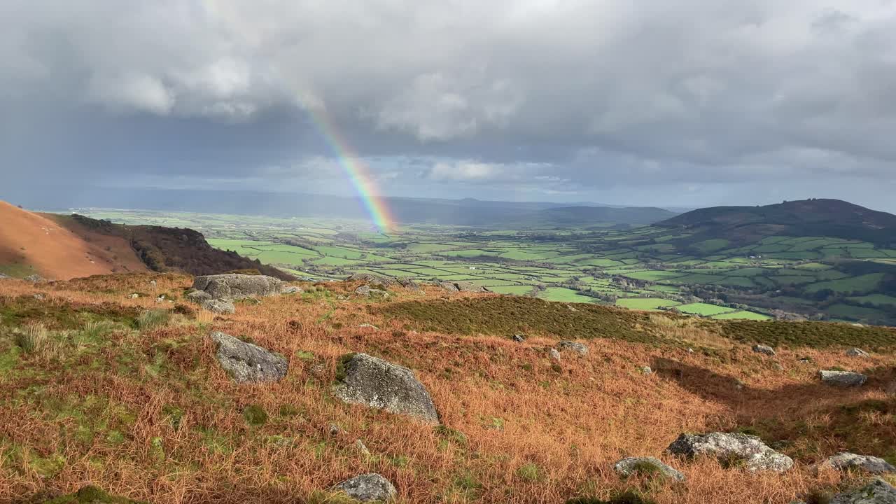 paisaje montañoso mirando a las fértiles tierras de cultivo de waterford irlanda con un arco iris y nubes de lluvia en invierno