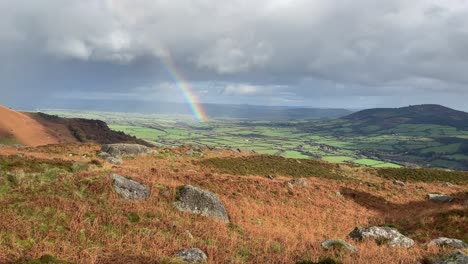 mountain landscape looking to the fertile farmlands of waterford ireland with a rainbow and shower clouds in winter