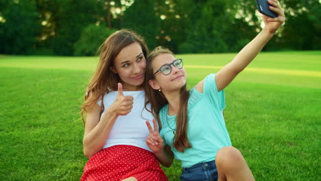 mujer y niña sentada en la hierba. hija tomando una selfie en el teléfono celular con la madre