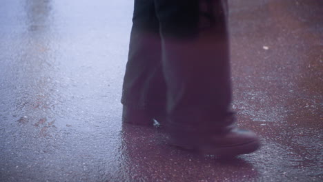 close-up of human leg in black trousers and boots walking calmly on wet ground during rainy weather, reflecting the rainy mood and wet surface, with focus on footsteps and surface details
