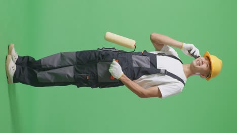 full body of side view asian man painter wearing safety helmet talking on smartphone and looking around while standing in the green screen background studio