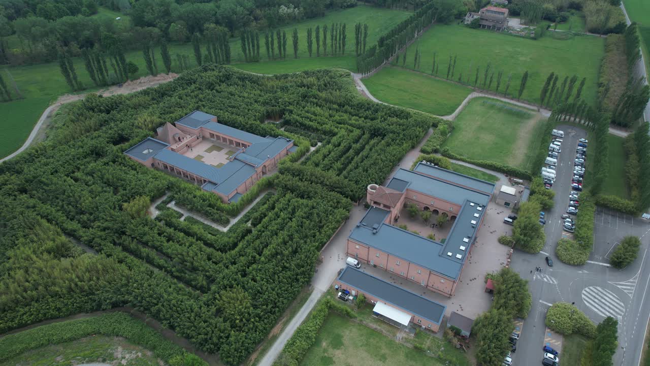 Labirinto della Masone a Fontanellato, provincia di Parma, che mostra un labirinto geometrico di bambù, un complesso museale con cortile neoclassico e un'area parcheggio nella campagna della Pianura Padana, ripresa statica