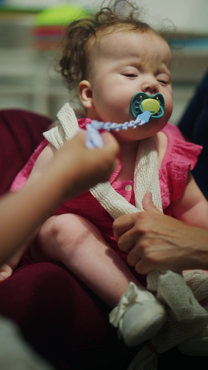 Close up of an infant resting in a supported position while the mother places a pacifier in the baby's mouth during a pediatric mobility and developmental therapy session