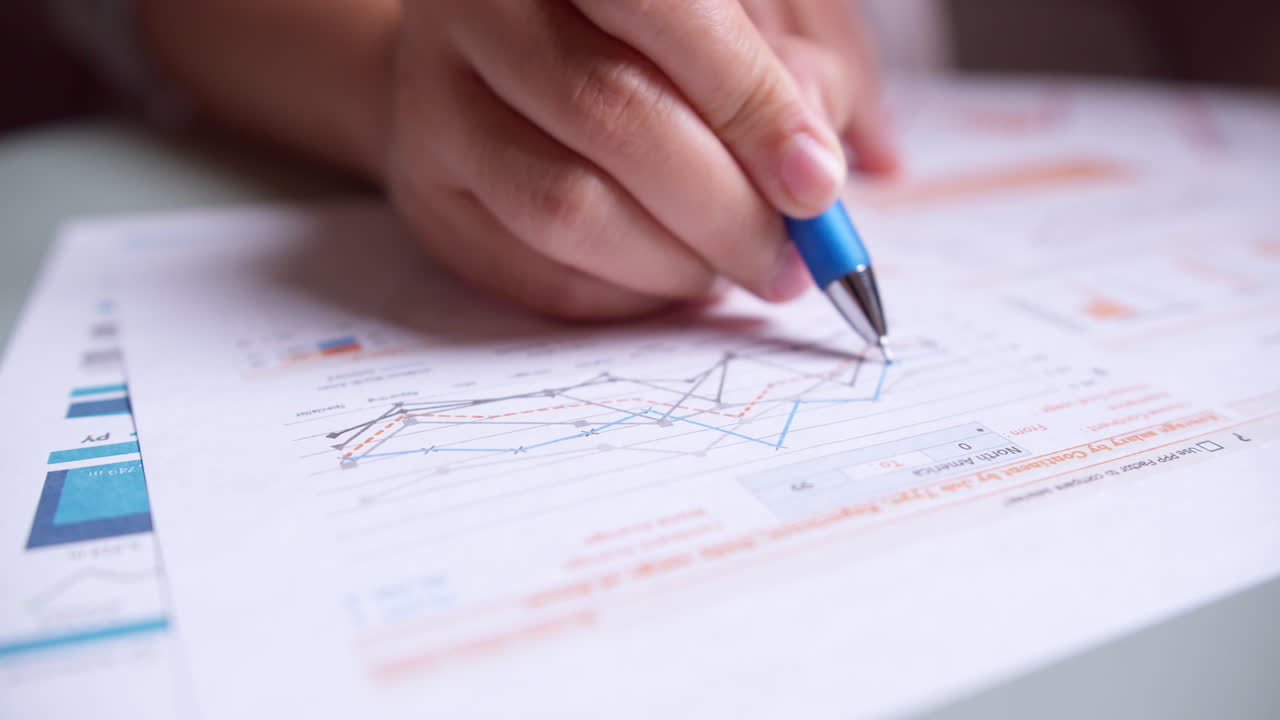 Close-up of businesswoman's hands with pen working at office desk and analyzing graphs and charts, profit report checking