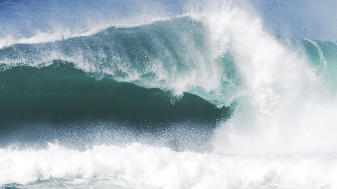 Backlit wave glows with fine mist and fluid texture as it barrels toward shore