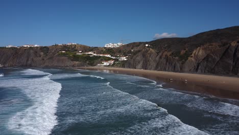 Drone-shot-of-people-in-the-sea-in-Arrifana,-Portugal-enjoying-the-life-on-a-bright-sunny-day-in-the-middle-of-december