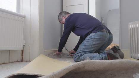 carpenter cutting and removing old carpet from room ready for replacement