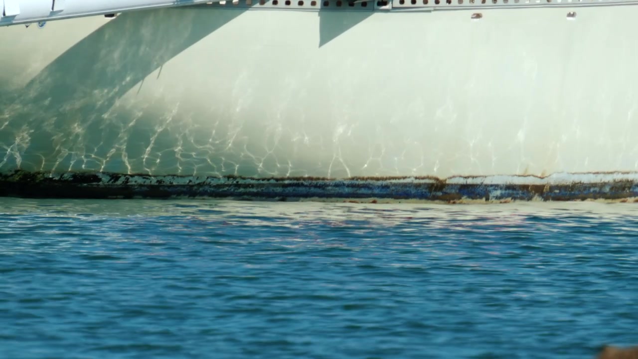 Scafo di yacht che mostra la linea di galleggiamento e incrostazioni marine con increspature dell'acqua che creano motivi sulla superficie