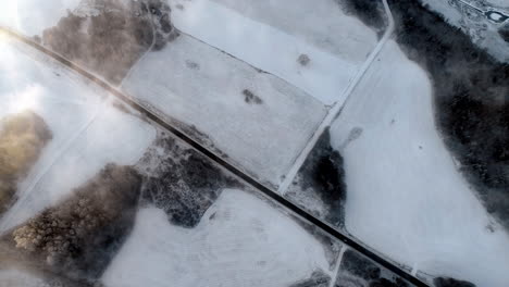 aerial drone flying above a road in the middle of a vast snow covered field on a cold winter morning with cars passing by on the road on a cloudy day