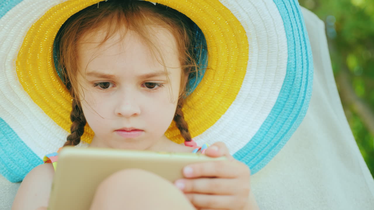 수영복을 입은 커다란 다색 모자를 쓴 귀여운 소녀가 안락의자에 앉아 놀고 있다