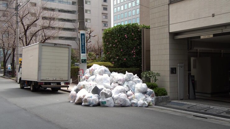 Inquadratura statica di sacchi di rifiuti accumulati su un marciapiede vicino a un furgone delle consegne a Tokyo
