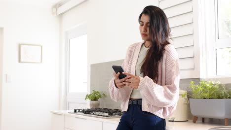 indian woman texting on smartphone in modern kitchen, enjoying leisure time, copy space