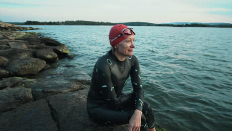 sportswoman in swimsuit sitting on lakeshore after training