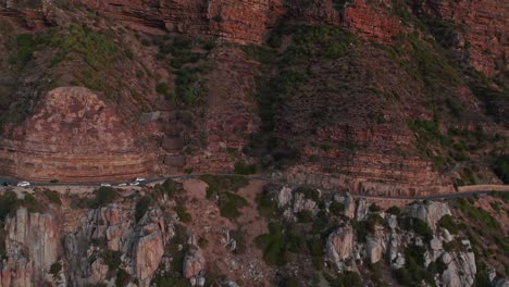 Vehículos-Circulando-Por-Chapman&#39;s-Peak-Drive,-Ciudad-Del-Cabo,-África-Al-Atardecer---Toma-Aérea-Con-Drones