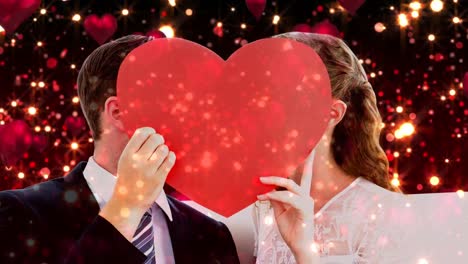 recién casados con un gran corazón rojo frente a sus caras