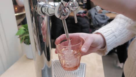 mujer vertiendo agua mineral en un vaso naranja de un hermoso dispensador cromado en el interior