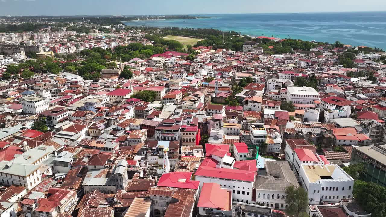 Ripresa cinematografica discendente con drone che vola all'indietro sopra i tetti di Stone Town, Zanzibar. L'architettura storica swahili, l'atmosfera costiera e la luce calda creano una scena senza tempo per viaggi e culto.