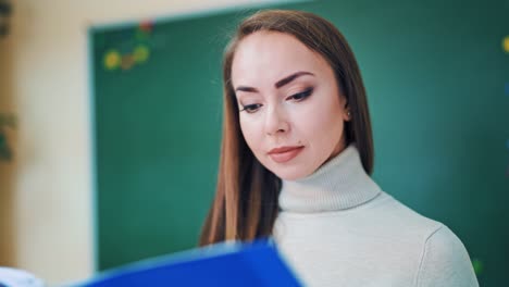 portrait of a beautiful teacher. lovely face of a young woman looking into a blue folder on the school board background. close-up.