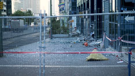 ground-level side view of a tel aviv street filled with broken glass and debris, seen through safety fences after an iranian missile strike.