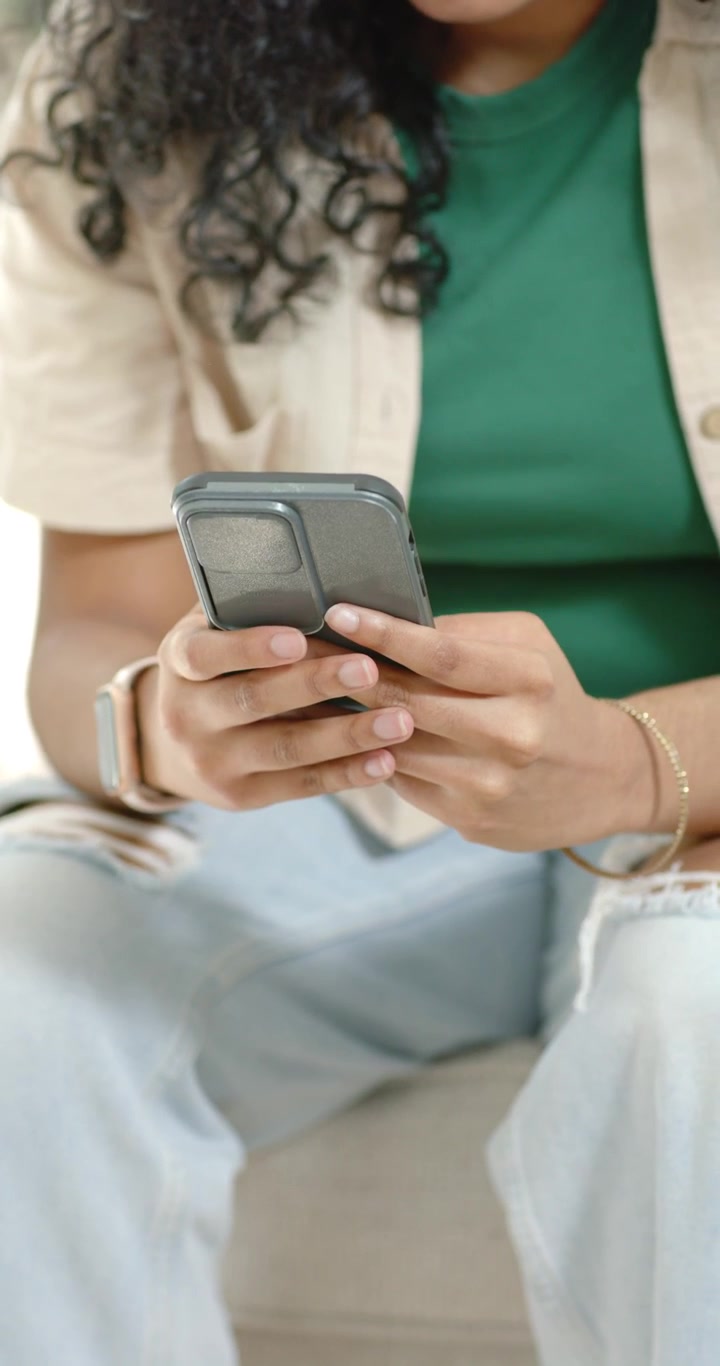 Video verticale: Donna che riceve una notifica, controlla lo smartphone, tocca e scorre sullo schermo mentre è sul divano